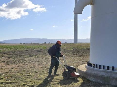Trabajador de Paisajismo La Rioja en la base de un aerogerenador realizando tareas de desbroce con una máquina